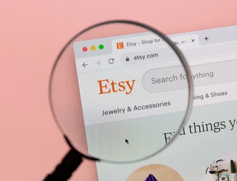 Eine Lupe über einem Browserfenster der Etsy-Website; Etsy-Logo, Suchfeld ('Search for anything') sichtbar.