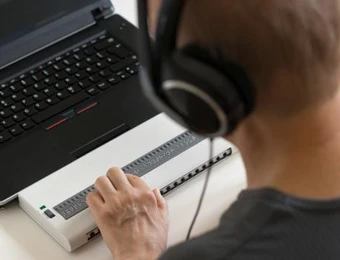 Person mit Kopfhörern vor Laptop, berührt externes Gerät mit vielen Tasten.