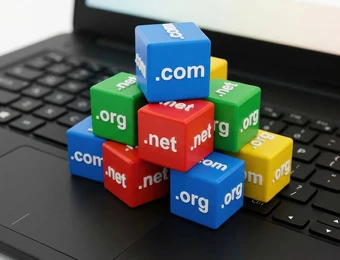 Mehrfarbige Würfel mit .com, .net und .org-Aufdruck stapeln sich auf einer Laptop-Tastatur.