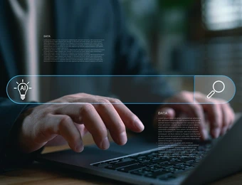 Hände tippen auf einem Laptop; eine blaue holografische Suchleiste mit Such-Icon erstreckt sich über die Tastatur.