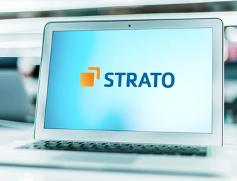 Offener Laptop auf hellem Tisch, Bildschirm zeigt STRATO-Logo in Blau mit orangefarbenem Quadrat.
