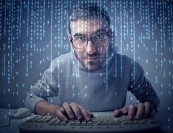 Mann mit Brille sitzt vor Tastatur, Hände darauf, aus dem oberen Bereich fallen blaue Binärcode-Zeilen.