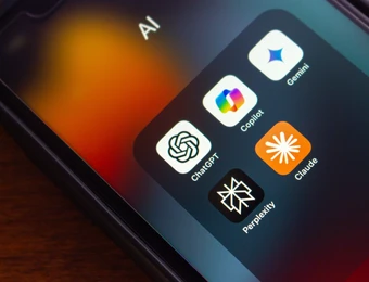 Nahaufnahme eines Smartphones mit einem Ordner, der App-Symbole von ChatGPT, Copilot, Gemini, Claude und Perplexity zeigt.