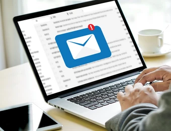 Laptop auf Tisch; Bildschirm zeigt blaues E-Mail-Icon mit rotem Benachrichtigungs-Punkt; tippen, Smartphone und Kaffeetasse