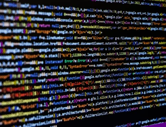 Nahaufnahme eines Monitors mit farbigem Quellcode; viele Zeilen Text in unterschiedlichen Farben auf dunklem Hintergrund.