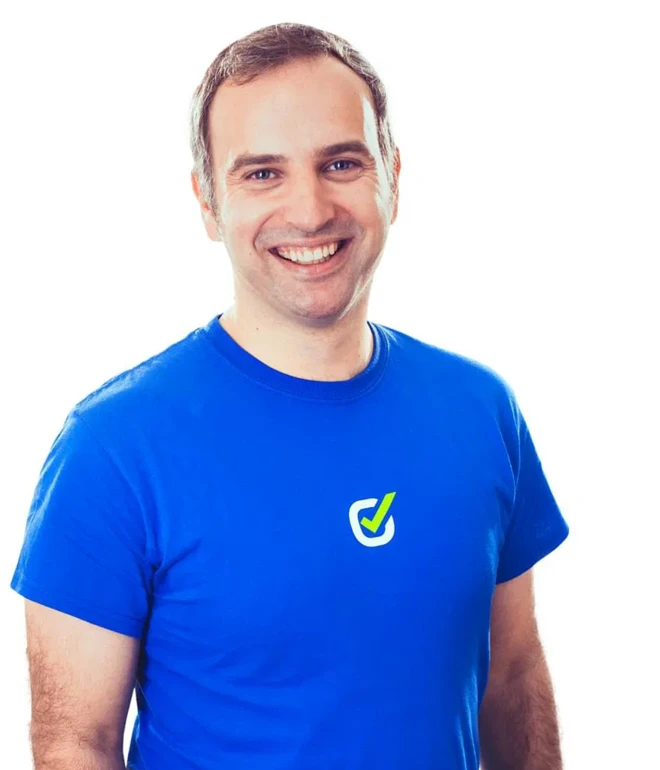 Mann in blauem T-Shirt mit kleinem Logo auf der Brust, lächelnd, weißer Hintergrund.