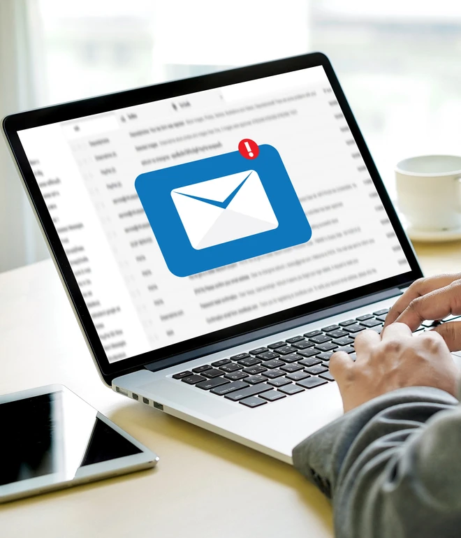 Laptop auf Tisch; Bildschirm zeigt blaues E-Mail-Icon mit rotem Benachrichtigungs-Punkt; tippen, Smartphone und Kaffeetasse