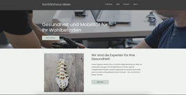 Website-Hero mit Logo Sanitätshaus Meier, Text Gesundheit und Mobilität; zwei Personen am Tisch, Spine-Modell auf Holzplatte.