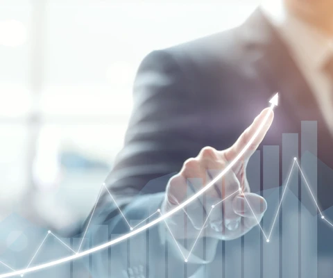 Person im Anzug zeigt auf eine transparente Diagramm-Grafik mit Kurve und Balken vor hellem Hintergrund.