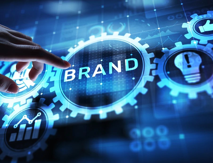 Eine Hand berührt leuchtend blaue Zahnräder; zentrales Zahnrad trägt BRAND, weitere Zahnräder mit Symbolen.
