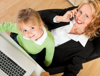 Eine Frau und ein Kind sitzen vor einem Laptop; die Frau hält ein Telefon am Ohr.