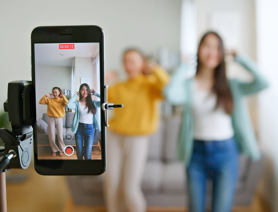 Smartphone auf Stativ filmt zwei Personen im Wohnzimmer; Display zeigt Aufnahme der beiden in Freizeitkleidung.