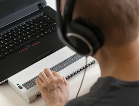 Person mit Kopfhörern vor Laptop, berührt externes Gerät mit vielen Tasten.