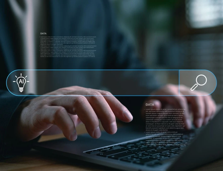 Hände tippen auf einem Laptop; eine blaue holografische Suchleiste mit Such-Icon erstreckt sich über die Tastatur.