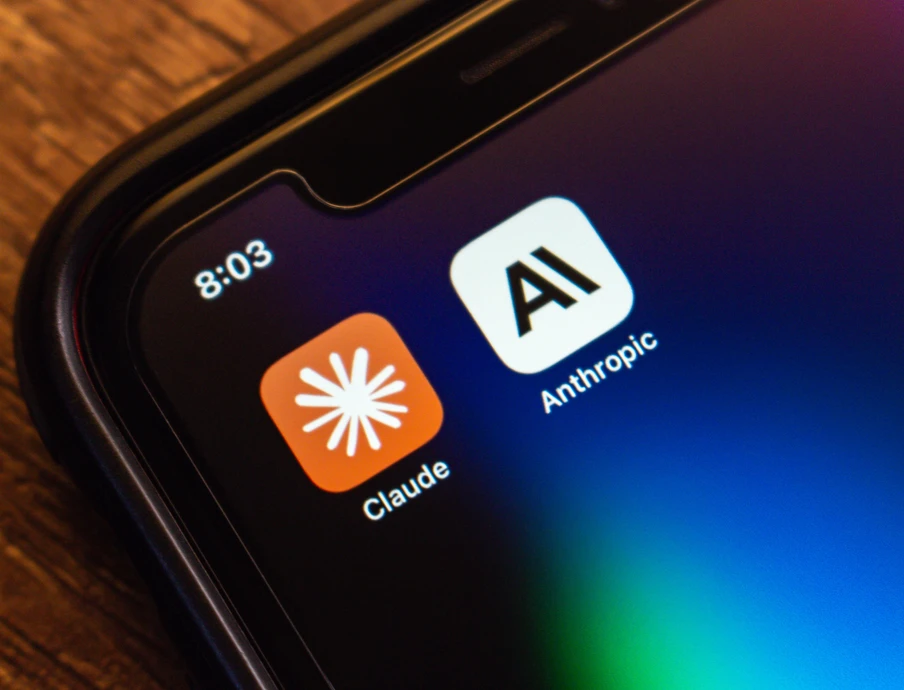 Nahaufnahme eines Smartphone-Bildschirms mit zwei App-Symbolen: Claude (orange, Sternblitz) und Anthropic (weiß, AI). Uhr 8:03