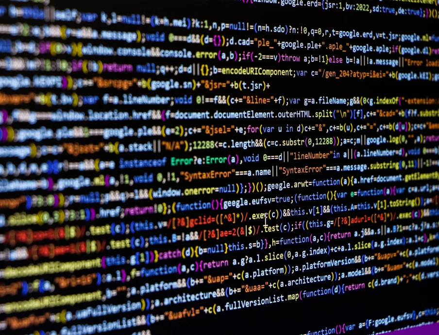 Nahaufnahme eines Monitors mit farbigem Quellcode; viele Zeilen Text in unterschiedlichen Farben auf dunklem Hintergrund.