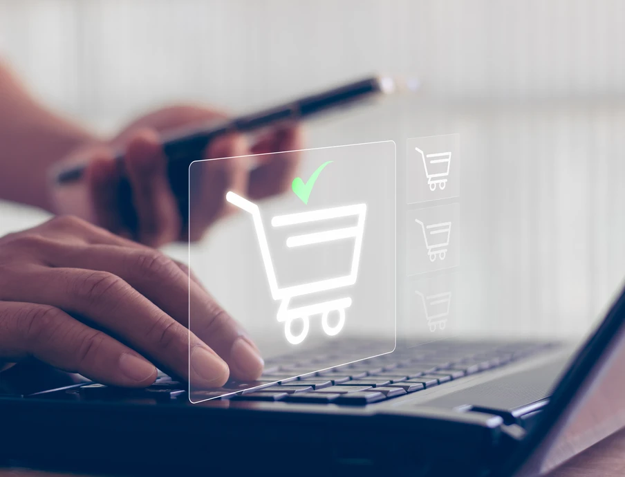 Nahaufnahme von Händen auf Laptop-Tastatur, mit durchsichtigen Einkaufswagen-Symbol und grünem Häkchen.