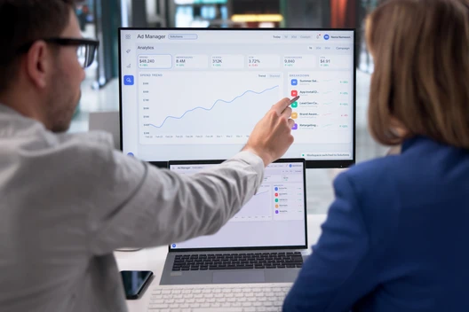 Zwei Personen schauen auf einen Monitor mit Diagrammen; eine zeigt auf die Grafik.