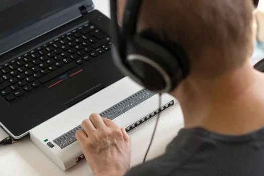 Person mit Kopfhörern vor Laptop, berührt externes Gerät mit vielen Tasten.