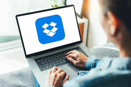 Person tippt auf Laptop; Bildschirm zeigt blaues Dropbox-Logo mit weißem Diamantsymbol.