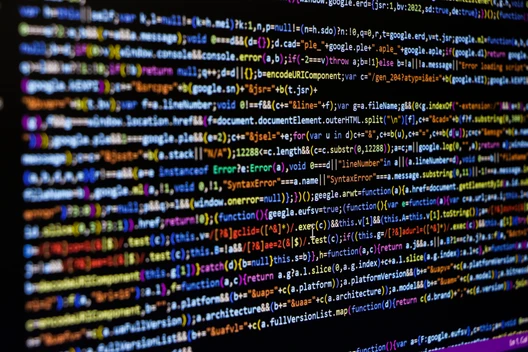 Nahaufnahme eines Monitors mit farbigem Quellcode; viele Zeilen Text in unterschiedlichen Farben auf dunklem Hintergrund.