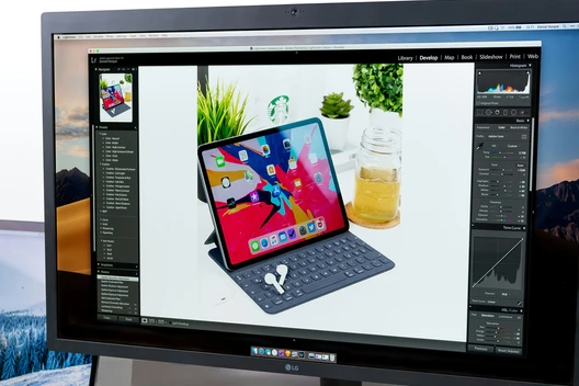 Monitor zeigt ein Foto eines iPad mit Tastaturhülle auf weißem Tisch; daneben Pflanzen.