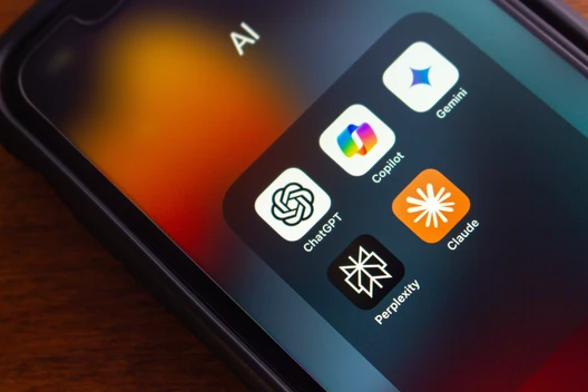 Nahaufnahme eines Smartphones mit einem Ordner, der App-Symbole von ChatGPT, Copilot, Gemini, Claude und Perplexity zeigt.